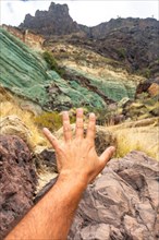Hand of a man at the natural monument at the Azulejos de Veneguera or Rainbow Rocks in Mogan, Gran