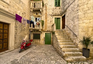 Laundry hanging over an alley with a red Vespa and green shutters, Trogir, Dalmatia, Croatia,