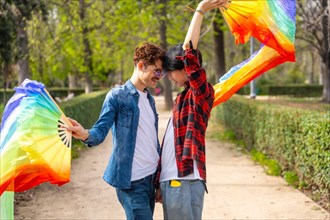 Side view of a multi-ethnic gay couple dancing using rainbow fans