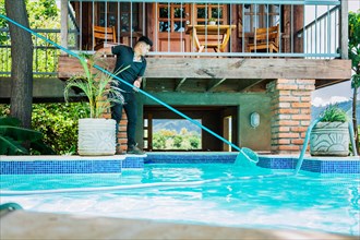 Man cleaning swimming pool water with a skimmer. Maintenance person cleaning the leaves of a pool