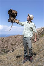Tourist holding an eagle in his arms, traditional Kyrgyz eagle hunt, near Bokonbayevo, Issyk Kul