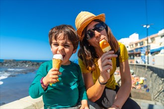 Mother with her little boy son enjoying summer vacation smiling eating ice cream by the sea
