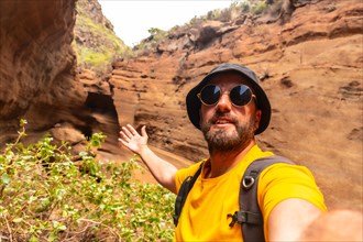 A man in a yellow shirt and sunglasses is taking a selfie in front of a rocky cliff. Concept of