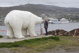 Polar bear sculpture in front of the town of Hammerfest with cruise ship Aida in the harbour,