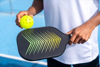 Unrecognizable close-up sportive man with pickleball equipment holding racket and yellow ball in an