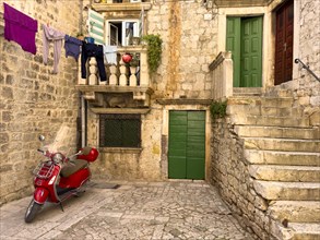 Red Vespa under a washing line in front of a traditional house, Trogir, Dalmatia, Croatia, Europe