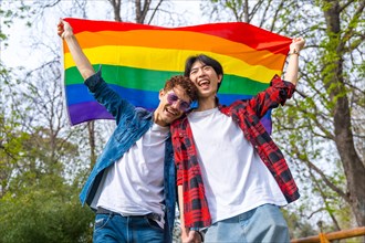 Low angle view portrait of a multi-ethnic gay couple raising lgbt flag in a park