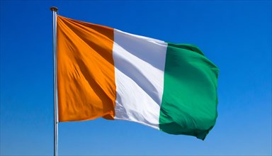 The flag of Ivory Coast flutters in the wind, isolated, against the blue sky