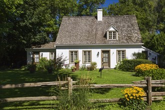 Old circa 1886 white with beige and brown trim Canadiana cottage style home facade with landscaped