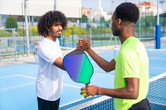Two african american young men shaking hands before playing pickleball in an outdoor court