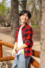 Vertical portrait of an asian gay man standing in a park smiling at camera