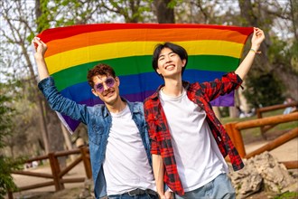 Portrait of a multi-ethnic gay couple raising a rainbow lgbt flag in a park