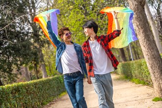 Happy multi-ethnic young gay couple raising LGBT rainbow colored fans in a park