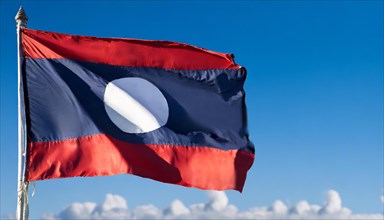 The flag of Laos flutters in the wind, isolated against a blue sky