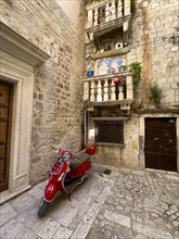 View down the alley to a red Vespa in front of a time-honoured building