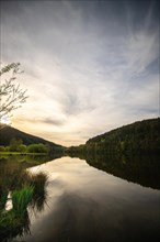 A lake in a landscape shot. A sunset and the natural surroundings are reflected in the water of the