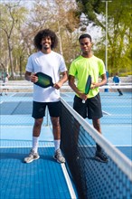 Vertical Portrait of two young african american pickleball players standing looking at camera