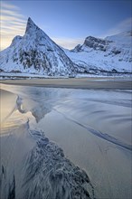 Steep mountain reflected in the water on the beach, coast, morning mood with clouds, winter, Senja,