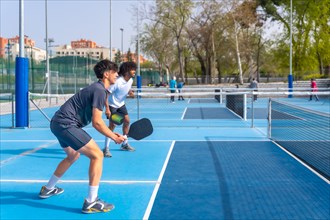 Full length side view of a multi-ethnic pickleball team playing with friends in an outdoor court