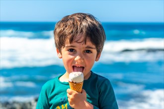 Portrait of a boy eating a delicious ice cream by the sea in summer. Family vacation concept