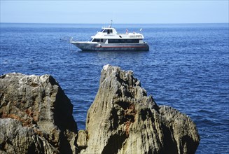 Excursion boat at the rocky coast of Capo Caccia with Grotta Nereo cave, Alghero, Sassari Province,