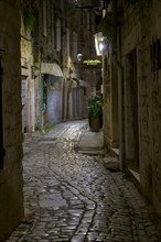 An illuminated alleyway with cobblestones and historic buildings at night, Trogir, Dalmatia,