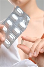 Close up view of fingers holding a pill in front of the package