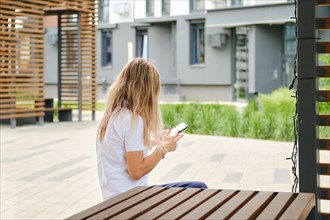 Back view of a woman in white shirt and sunglasses on bench with smartphone