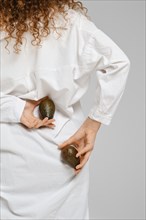 Female hands hold two whole avocado behind her back