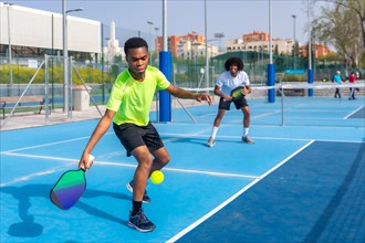African young friends playing pickleball in an outdoor court in a sunny day
