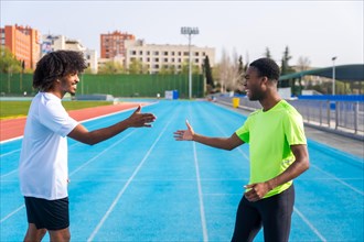 Side view of two african american young happy runners high-fiving in a running track