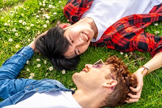 Top side view of a multiracial young gay couple in love lying on the grass looking at each other
