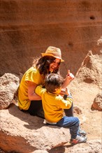 A woman and a child are sitting on a rock in a desert. The woman is wearing a yellow shirt and a