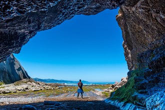 Man hiker in the Algorri cove sea cave on the flysch coast of Zumaia, Gipuzkoa. Basque Country