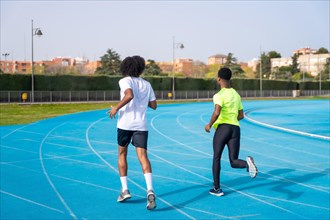 Rear view of two african american young runners training together in a running track