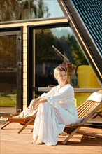 Woman sitting on wooden folding chair on terrace of a-frame cabin and looking to the side