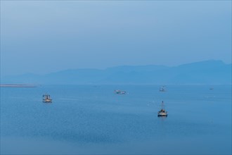 Several fishing boats float peacefully on calm water during the serene blue hour of dusk, in South