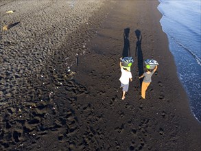 2 woman carry the freshly caught fish in the morning over the black lava beach of Amed, Karangasem