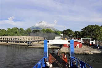 Lake Nicaragua, Ferry on the shore of a lake with an active volcano in the background and cloudy