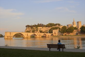 Woman on a park bench on the banks of the Rhone, Pont Saint Benezet bridge, Papal Palace and