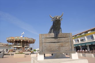 Statue of a Camargue bull and carousel, Les Saintes-Maries-de-la-Mer, Camargue, Bouches-du-Rhone,