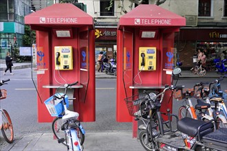 Shanghai, China, Two red telephone booths on a pavement next to parked bicycles, Shanghai, People's