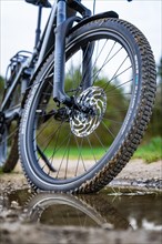 Close-up of a bicycle tyre in front of a puddle with reflections, spring, e-bike forest bike,