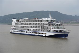 Cruise ship on the Yangtze River, White and blue cruise ship on a river with a slightly cloudy sky