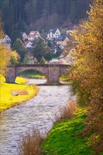 An old stone bridge over a river with a view of houses on the bank, spring, Calw, Black Forest,