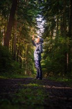 A hiker raises his hand in greeting or to block the sunlight in the dense forest, Calw, Black