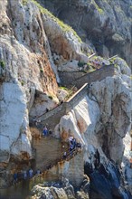Stairs with visitors on the outside of the Capo Caccia cliff near Grotta Nereo cave, Alghero,