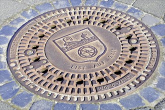List, A manhole cover with engraved coat of arms and lettering, surrounded by paving stones, Sylt,