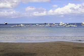 San Juan del Sur, Nicaragua, A group of boats on a calm sea in front of a beach under a cloudy sky,