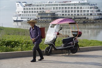 Cruise ship on the Yangtze River, A man walks next to an electric rickshaw, in the background a